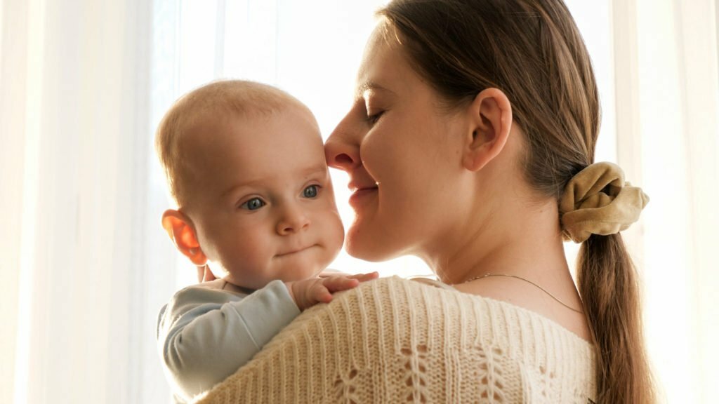 Portrait of little baby and smiling mother hugging at home. Concept of family happiness and parenting